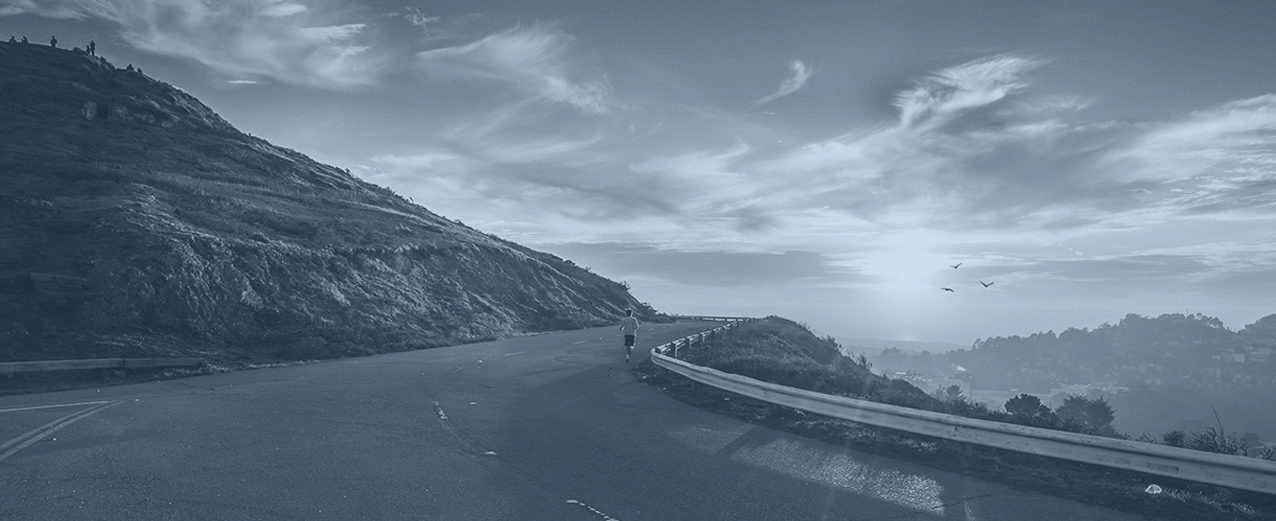 A runner on an open road above a hilly town